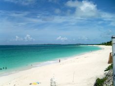 people are on the beach and in the water near the shore with blue skies above