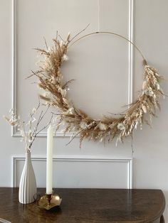 a wreath with dried flowers is on a table next to a candle and two vases