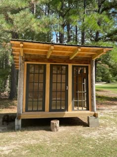 a small wooden cabin in the middle of a forest with doors open and windows on each side