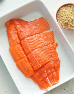 two pieces of raw salmon on a white plate next to a bowl of seasoning