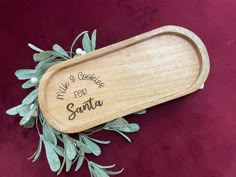 a wooden tray with writing on it sitting on a red velvet surface next to some green leaves