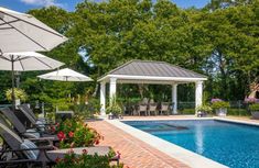 an outdoor swimming pool with patio furniture and umbrellas around it, surrounded by trees