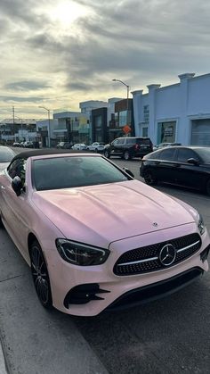 a pink mercedes benz coupe parked in a parking lot next to other cars and buildings