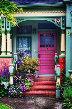 a pink door is on the side of a green house with red steps and flowers