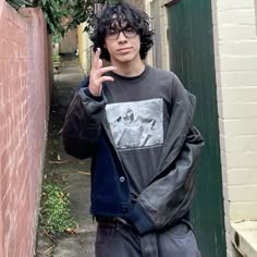 a young man is making the peace sign with his hand while standing in an alleyway