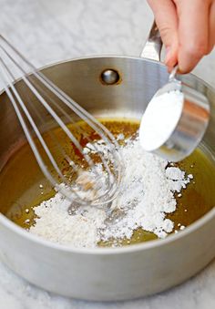 a person whisking flour into a metal bowl