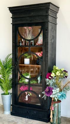 a black china cabinet with flowers and plants in it