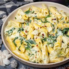 a white bowl filled with pasta and spinach on top of a blue table cloth