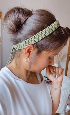 a woman wearing a green headband and holding her hand up to her face while looking down