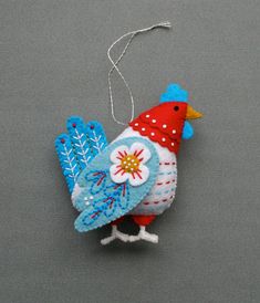 an ornament shaped like a chicken on a gray surface with white dots and blue feathers