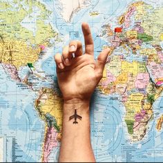 a person's hand with a small airplane tattoo on their left wrist and the world map in the background