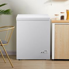 a white chest freezer sitting next to a wooden cabinet in a room with a potted plant