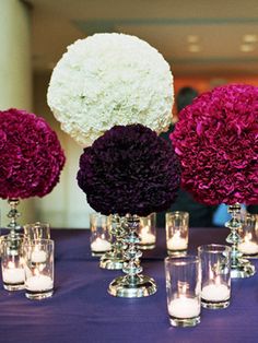 purple and white flowers are arranged in vases on a table with silver candlesticks