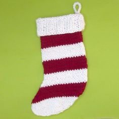 a red and white knitted christmas stocking hanging on a green wall next to a plate