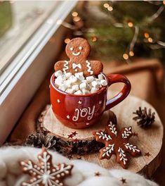 a cup filled with marshmallows sitting on top of a wooden slice next to a window