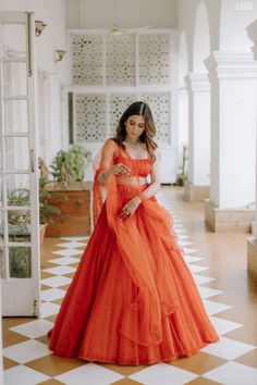 a woman in an orange dress standing on a checkered floor looking at her cell phone