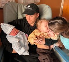 a man sitting in a chair with two women and a baby, both holding their babies