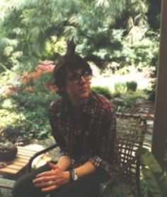 a man sitting on a wooden bench in front of a tree and plant filled area