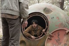 a man standing next to a giant object in the woods with another person looking at it