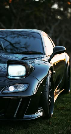 the front end of a black sports car parked on top of a lush green field