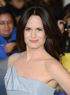 a woman in a gray dress posing for the camera with people behind her taking pictures