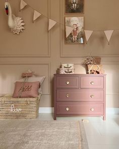 a pink dresser sitting in a room next to a wall with pictures and bunting