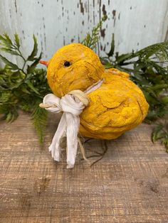 a small yellow bird sitting on top of a wooden table next to green plants and greenery