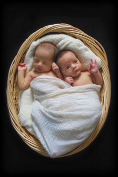 two baby babies are laying in a wicker basket on top of each other, wrapped in white blankets