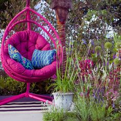 a pink hanging chair in the middle of a garden with purple flowers and plants around it