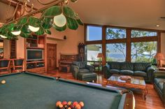 a pool table in the middle of a living room with couches and lamps hanging from the ceiling