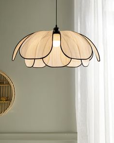 a light fixture hanging from the ceiling in a room with white curtains and a bird cage behind it