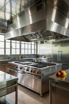 an industrial kitchen with stainless steel appliances and fruit on the counter top, in front of large windows