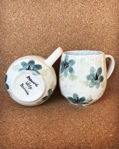 two tea cups sitting on top of a brown table next to each other with blue flowers painted on them