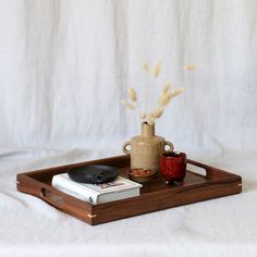 a wooden tray with a coffee cup and book on it, next to a vase