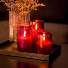 four red candles sitting on top of a tray next to a vase filled with flowers