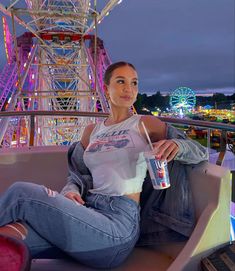 a woman sitting on top of a roller coaster holding a drink in her right hand