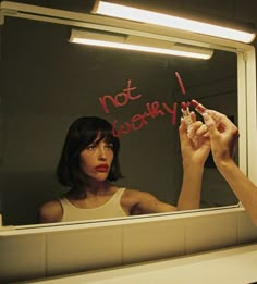 a woman is writing on the mirror while holding a lipstick in front of her face