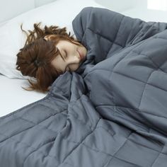 a woman laying in bed under a gray blanket and covering her face with the comforter