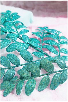 green glittered leaves are sitting on a white surface with pink flowers in the background