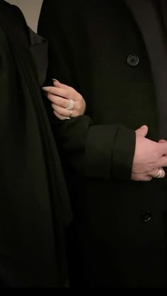 a woman wearing a black coat and holding onto another person's arm with her hand