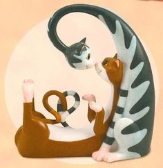 a couple of cats sitting next to each other on top of a cat statue in front of a white circle