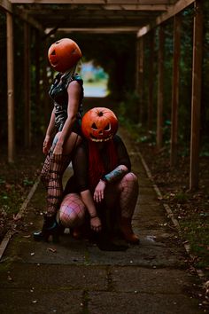 two women with pumpkins on their heads are sitting in the middle of an alley way