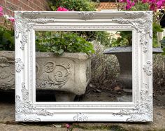 a white frame sitting on top of a sidewalk next to flowers and potted plants