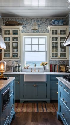 a kitchen with blue cabinets and white counter tops next to a window overlooking the ocean