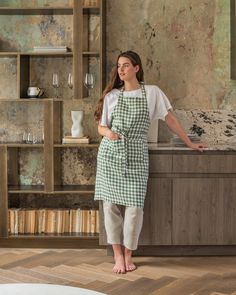 a woman standing in front of a kitchen counter with an apron over her shoulder and legs crossed