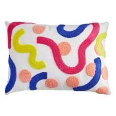 a white pillow with multicolored circles and dots on the front, sitting on a white surface