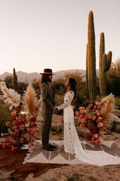 a man and woman standing next to each other in front of a cactus plant with flowers