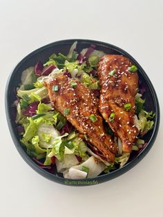 two pieces of chicken on top of a salad with sesame seeds and lettuce