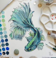 a drawing of a fish on paper next to watercolor paints