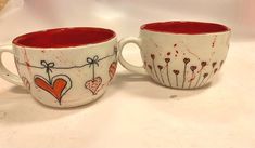 two coffee mugs decorated with hearts and flowers on a white counter top next to each other